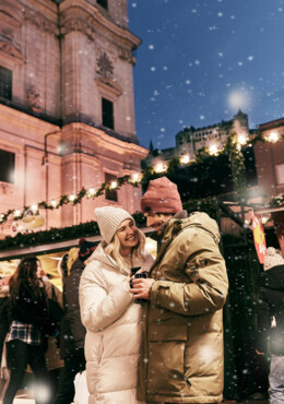 Ein Paar spaziert gemeinsam über den Christkindlmarkt und trinkt Glühwein.