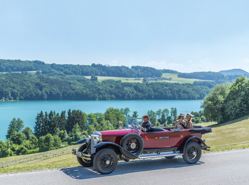 Ein roter Oldtimer fährt die idyllischen Straßen am See entlang